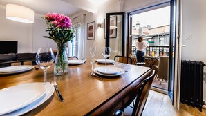 A dining area with a wooden table set for four, a vase of flowers, and a view of the city through an open door. - ZABALETA SUITE: 6 PAX Superior apartment. Practical and distinguished. 500 meters from the beach (San Sebastián)
