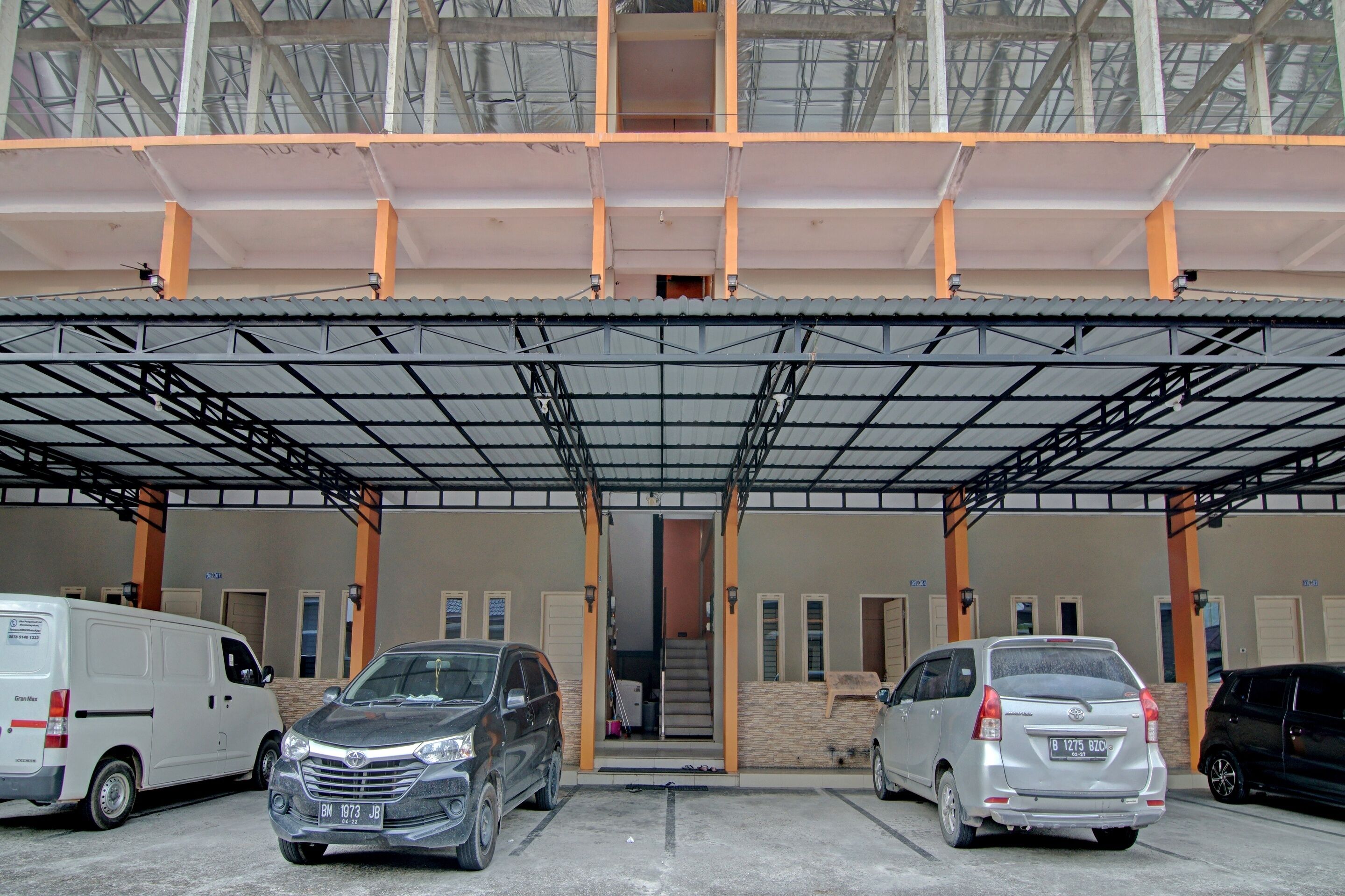 A covered parking area with multiple vehicles, including a white van, a gray SUV, and a silver sedan.