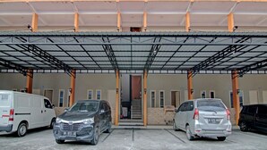 A covered parking area with multiple vehicles, including a white van, a gray SUV, and a silver sedan. - OYO 91949 Ameera Homestay Syariah (Pekanbaru)
