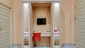A room with a wooden wardrobe, a desk with a chair, a bed, and a television. - OYO 91949 Ameera Homestay Syariah (Pekanbaru)