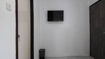 Un dormitorio con una cama, un televisor montado en la pared, un cesto de basura y un armario.