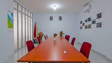 Un salón de conferencias con una larga mesa, sillas rojas, un jarrón de flores y banderas.