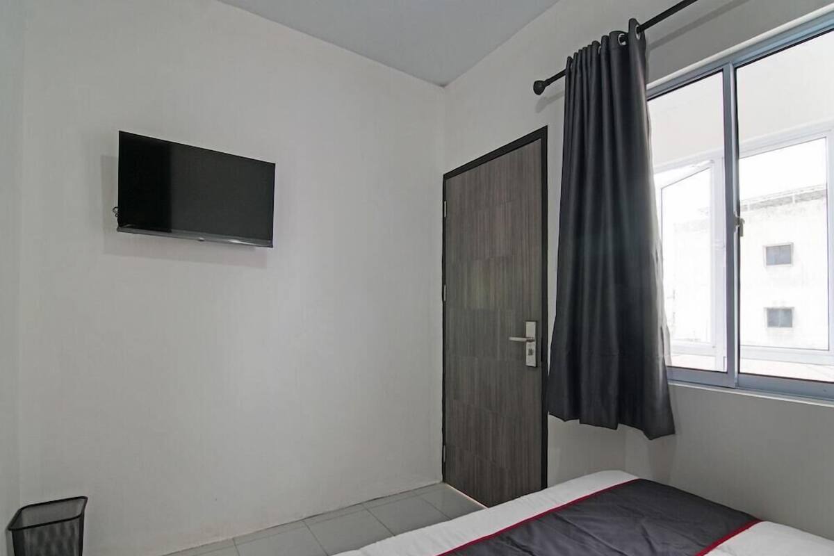A bedroom with a bed, a TV mounted on the wall, a door, and a window with curtains.