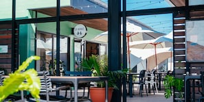 An outdoor seating area with tables and chairs, potted plants, and umbrellas.
