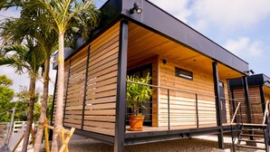 Una cabaña de madera moderna con balcón, una planta en maceta y una escalera.