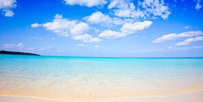 A beach with clear turquoise water and a sandy shore under a blue sky with scattered clouds. - Hotel Local Base (Miyakojima)