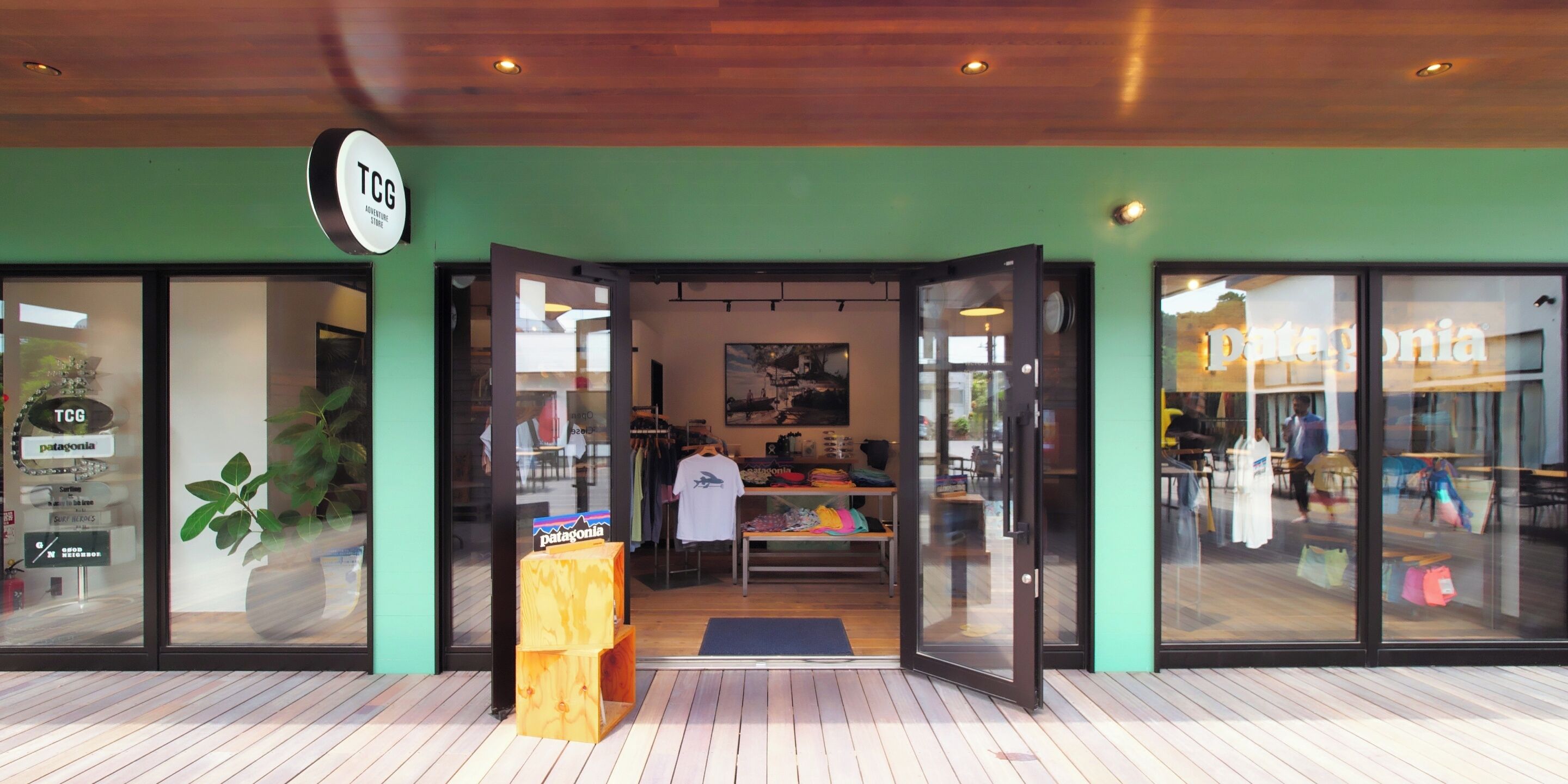 A storefront with a green facade, a wooden display stand, and a sign reading "TCG".