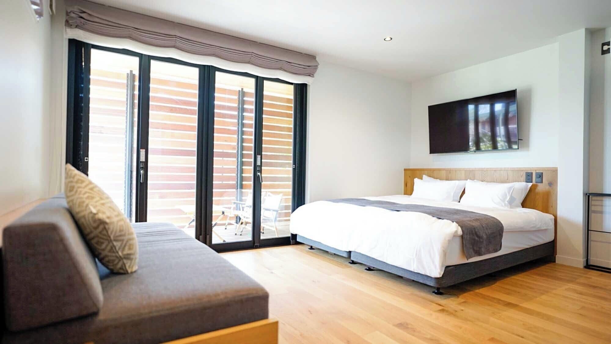 Un dormitorio con cama, sofá, televisor y puerta corrediza de cristal al exterior.