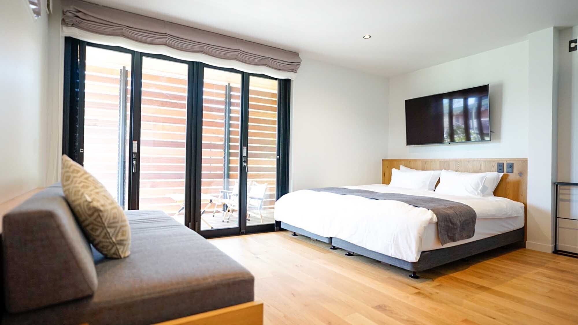 Un dormitorio con cama, sofá, televisor y puerta corrediza de vidrio al exterior.