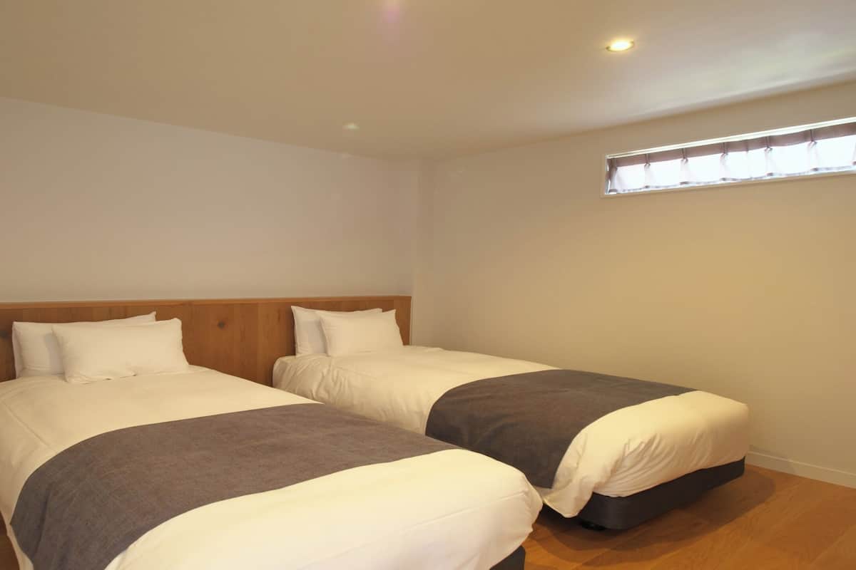 A hotel room with two single beds, wooden headboards, and a small window with curtains.