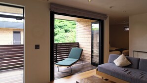 Una sala de estar moderna con un sofá, un sillón y un ventanal corredero que da a una terraza al aire libre.
