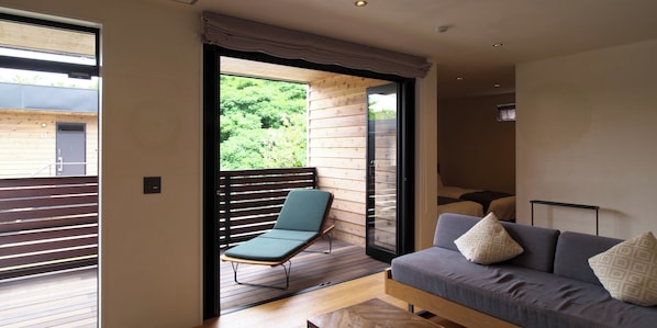 A modern living room with a sofa, a lounge chair, and a sliding glass door leading to an outdoor deck. - Hotel Local Base (Miyakojima)