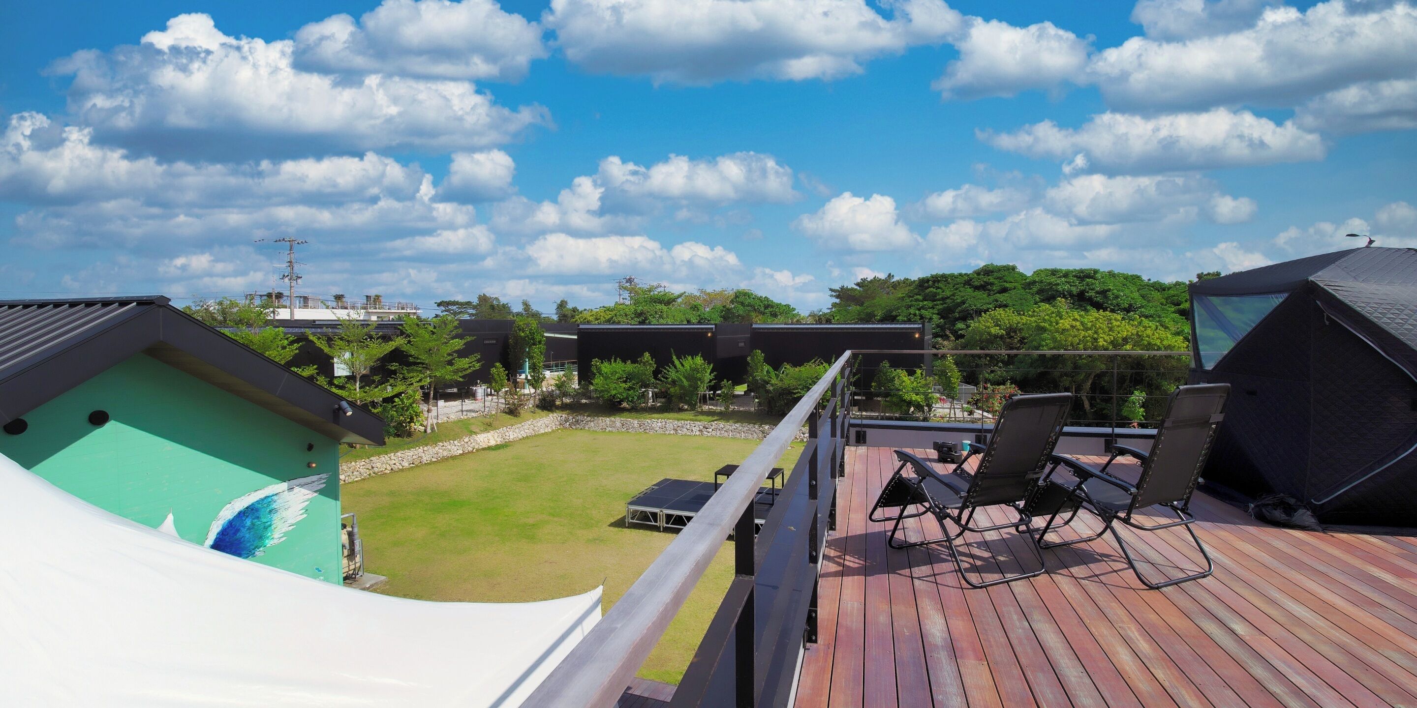 A deck with two lounge chairs and a small table, overlooking a grassy area with a view of a building and trees in the background.