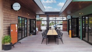 Un espacio exterior para comer con una larga mesa de madera y sillas, rodeado de puertas y ventanas de vidrio.