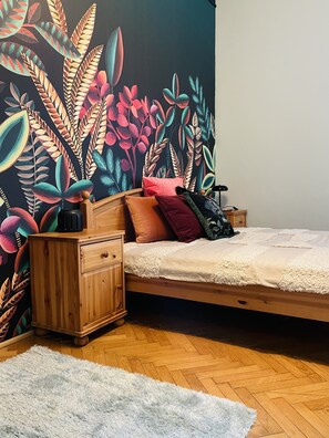 Un dormitorio con cama, mesita de noche de madera y un mural de pared colorido.