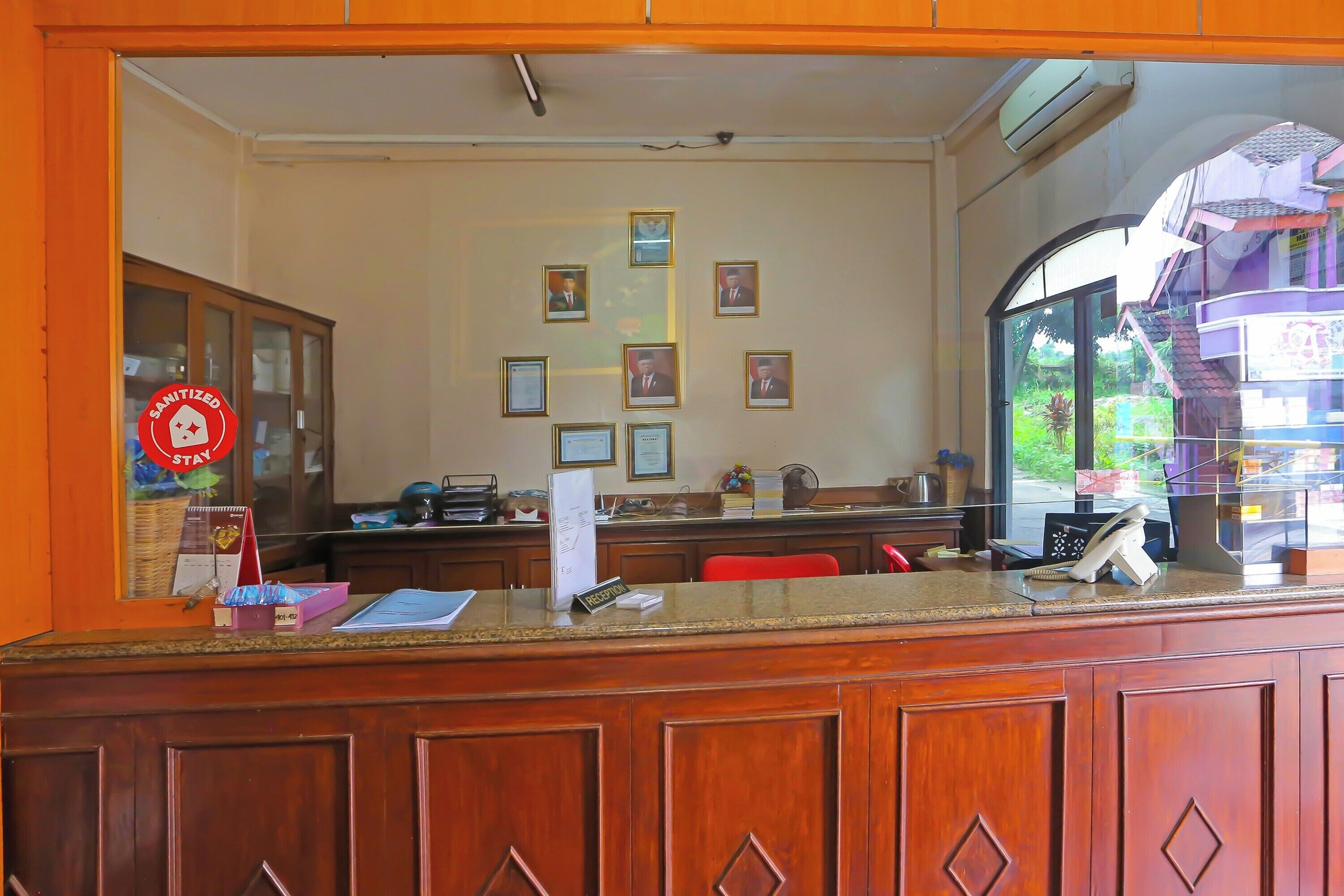 A reception desk with framed certificates on the wall, a wooden counter, and a window with a view of greenery outside.