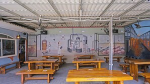 Café con mesas y bancos de madera, un mural en la pared y un cartel que indica servicio de café y bebidas sin alcohol.