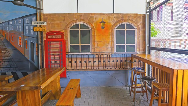 Zona de bar con bancos y taburetes de madera, una cabina telefónica roja y un mural con una escena callejera.