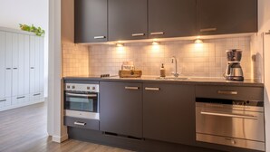 A modern kitchen with dark cabinets, a built-in oven, a dishwasher, and a coffee maker. - Apartment with balcony on the sunny side, close to nature and beach. (Oostkapelle)