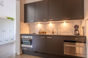 Eine moderne Küche mit dunklen Schränken, einem eingebauten Backofen, einem Geschirrspüler und einer Kaffeemaschine.