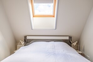 Ein Schlafzimmer mit Dachfenster, einem Bett, Nachttischlampen und einem Nachttisch.