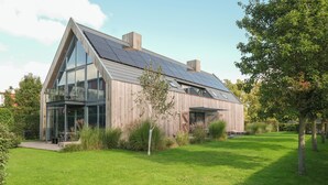 A modern house with a sloped roof, large windows, and solar panels. - Apartment with balcony on the sunny side, close to nature and beach. (Oostkapelle)