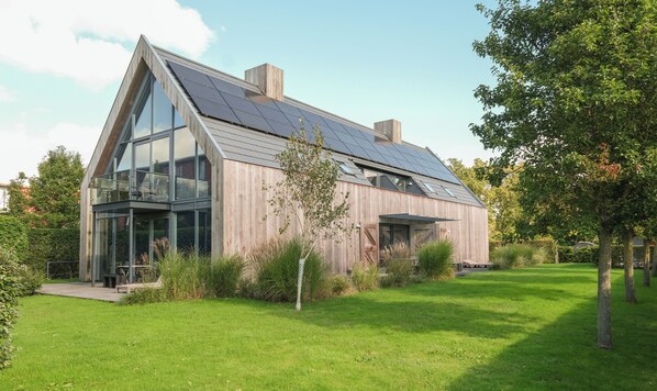 A modern house with a sloped roof, large windows, and solar panels.