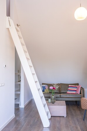 A modern interior with a white staircase, a sofa with colorful cushions, and a vase with flowers.