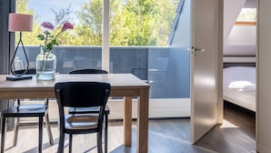 A modern room with a wooden table, two chairs, a vase with flowers, a lamp, and a bed with a skylight. - Apartment with balcony on the sunny side, close to nature and beach. (Oostkapelle)