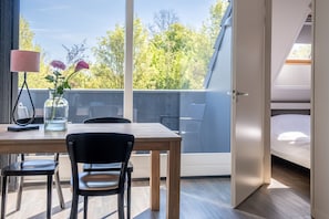A modern room with a wooden table, two chairs, a vase with flowers, a lamp, and a bed with a skylight. - Apartment with balcony on the sunny side, close to nature and beach. (Oostkapelle)