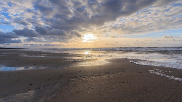 A beach with a sunset, clouds, and a distant pier. - Apartment with balcony on the sunny side, close to nature and beach. (Oostkapelle)