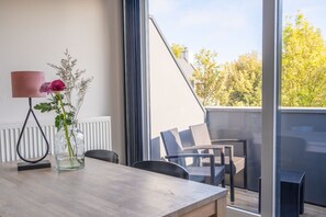 A dining area with a table, chairs, a vase with flowers, and a view of the outside.