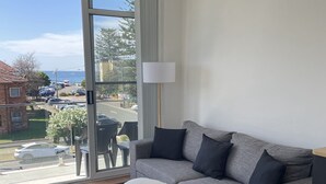 Een moderne woonkamer met een grijze bank, een witte poef en een vloerlamp.