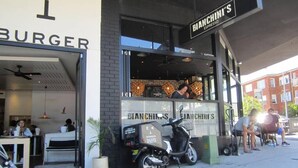 Een restaurant met een bord waarop "BIANCHINI'S ESPRESSO" staat en een bezorgscooter voor de deur.