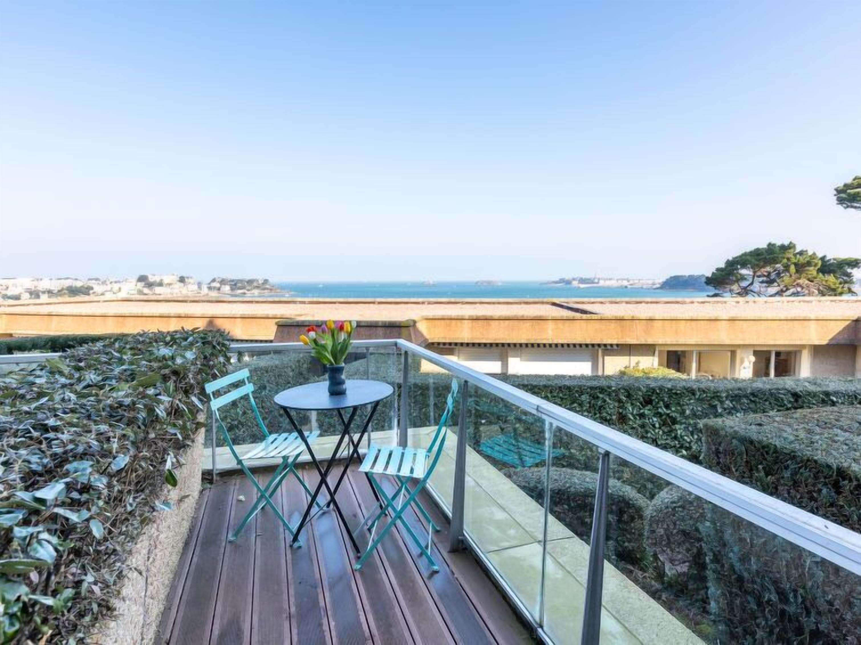 A balcony with a table and chairs, overlooking a coastal view.