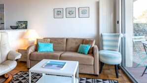 A modern living room with a beige sofa, a white coffee table, and a striped armchair. There are framed artworks on the wall and a window providing a view outside. - Le Parc de La Ronceray by Interhome (Dinard)
