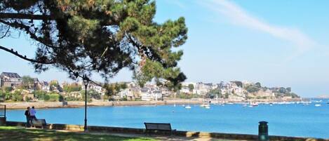 Un parque costero con césped, bancos y vistas al mar con barcos.