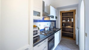 Une cuisine compacte avec des meubles blancs, une cuisinière à gaz et un dosseret de carrelage bleu.