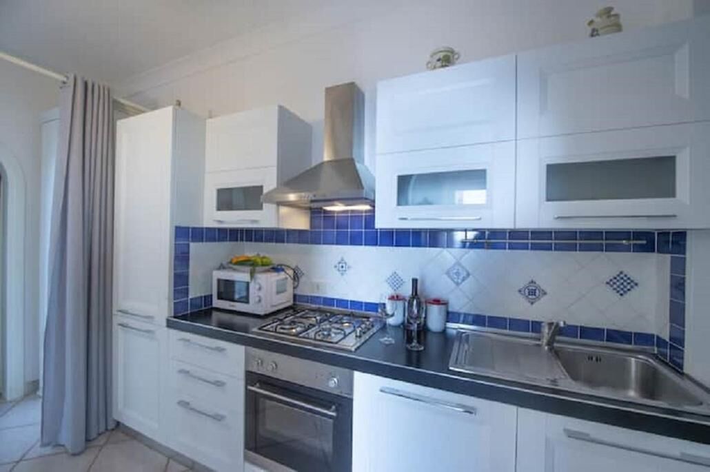 A kitchen with white cabinets, a gas stove, a microwave, and blue-tiled backsplash.