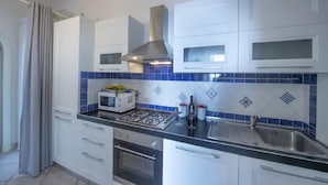 Une cuisine avec des meubles blancs, une cuisinière à gaz, un four à micro-ondes et un dosseret de carrelage bleu.