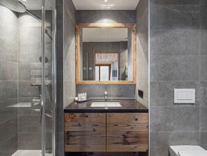 A modern bathroom with a glass shower enclosure, a wooden vanity, and a large mirror. - Spacious chalet in Courchevel with pool and sauna (Courchevel)