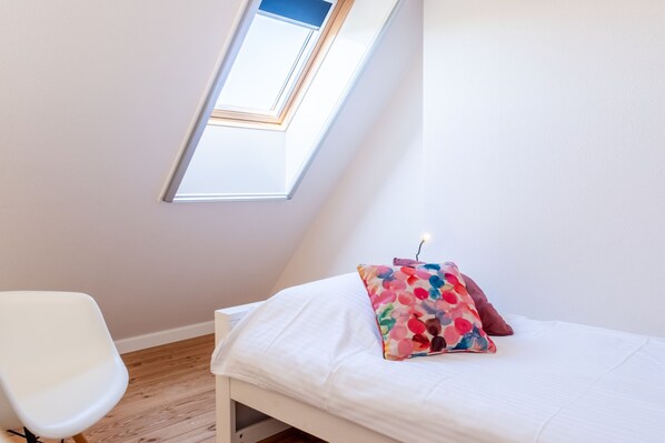 A room with a bed, a white chair, and a skylight. - A beautiful and comfortable apartment within walking or biking distance of the forest, dunes, and beach. (Oostkapelle)