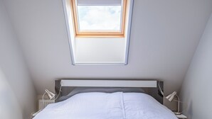 Una camera da letto con finestra sul tetto, un letto, lampade da comodino e un comodino.
