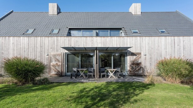 Un edificio moderno con tetto grigio, facciata in legno e un patio con mobili da esterno.