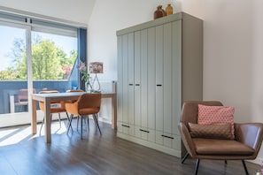 A dining area with a table and chairs, a cabinet, and a chair with a cushion. - Beautiful and comfortable apartment within walking/biking distance of forest, dunes and beach. (Oostkapelle)