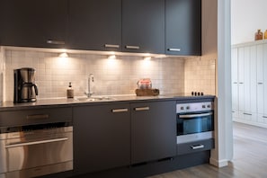 Eine moderne Küche mit dunklen Schränken, einem Einbauofen, einer Kaffeemaschine und einem Spülbecken.