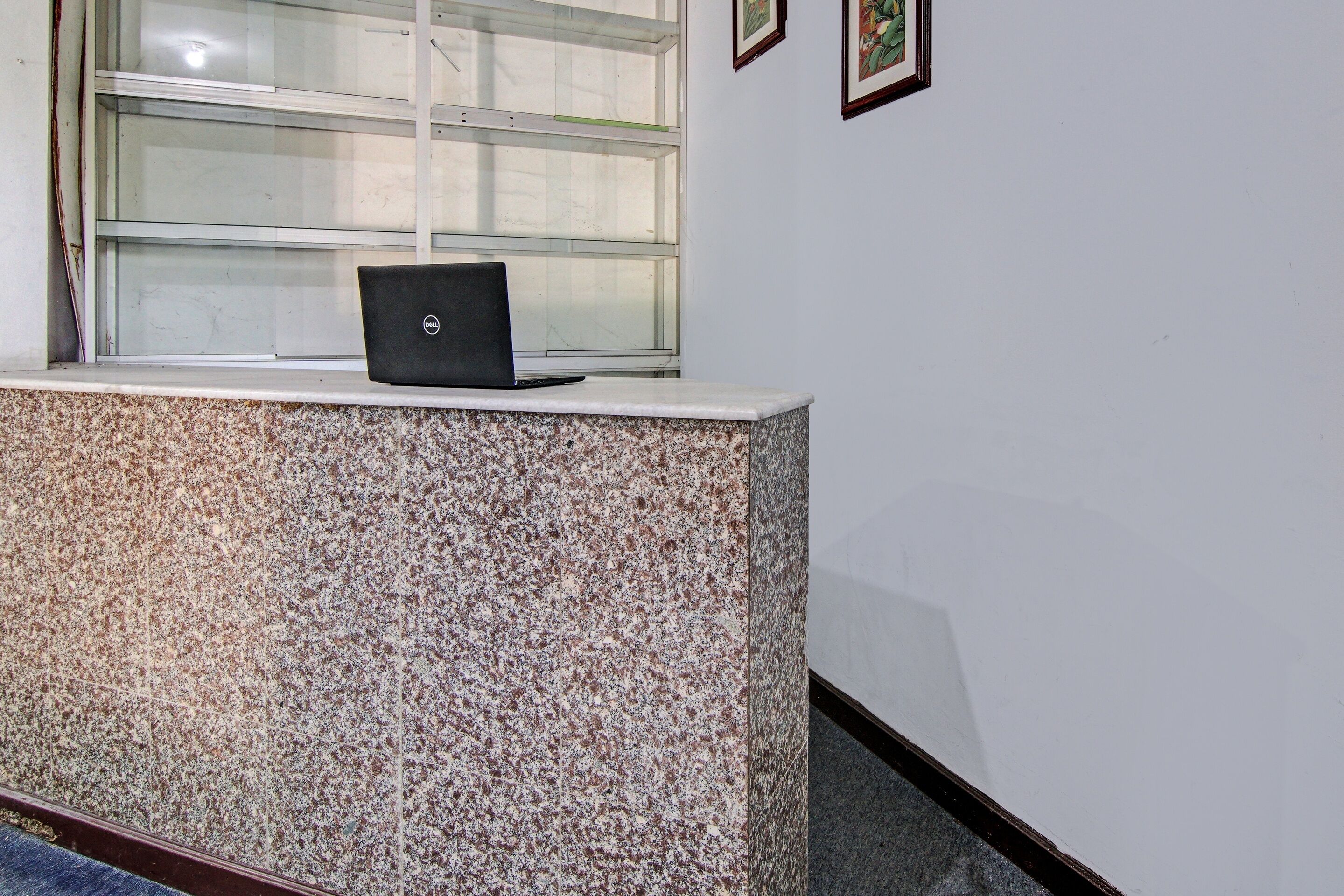 A reception desk with a laptop, a window, and framed pictures on the wall.
