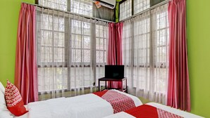 Une chambre d’hôtel avec un grand lit, une télévision et une fenêtre avec des rideaux légers.