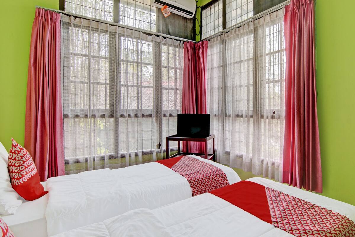 A hotel room with a large bed, a TV, and a window with sheer curtains.