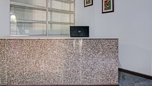 Un comptoir d’accueil avec un ordinateur portable, une fenêtre et deux tableaux encadrés au mur.